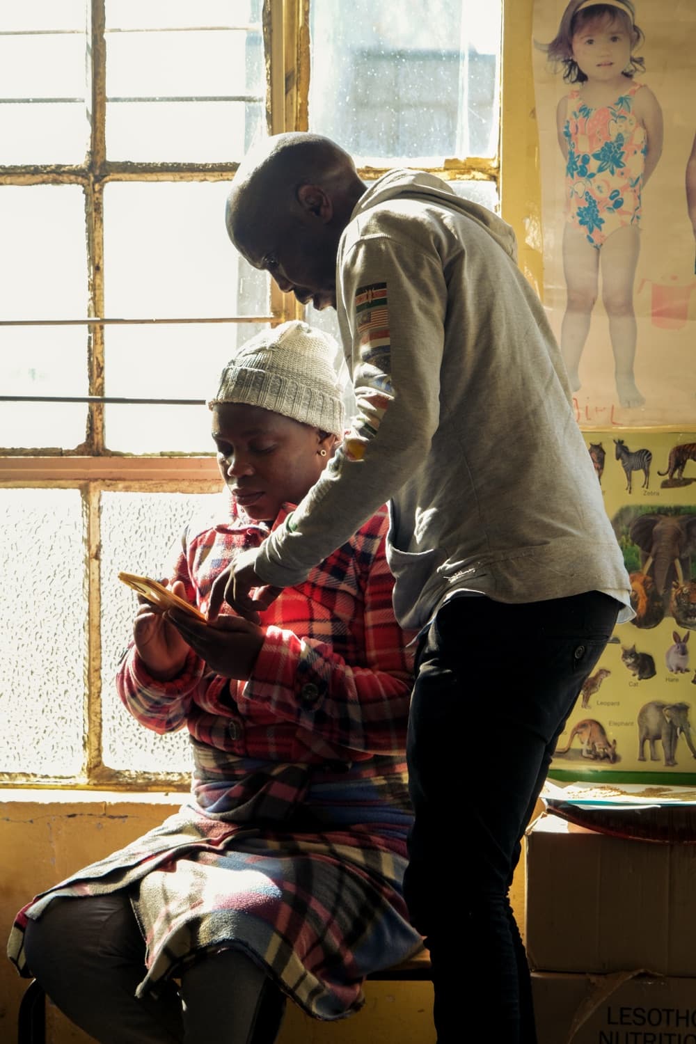 One person showing another how to use Luma on a phone in a sunlit classroom